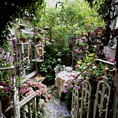 A view onto a white metal banister and a romantic courtyard with a terrace table between green plants