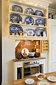 Blue and white dishes on a built-in kitchen shelf hung with a chain of lights and Oriental tiles decorating a niche where the gas oven stands