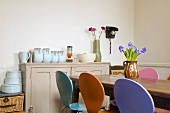 Coloured chairs at a dining table and storage jars on a wooden country-style chest of drawers