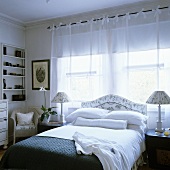 A naturally lit bedroom with a double bed in front of a window and light curtains