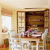A dining table laid in front of an open glasses cabinet