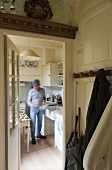 A view from a cloakroom through an open door into a white fitted kitchen where a man is cooking
