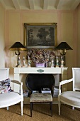 Baroque chairs and a foot stool in front of a white shelf and a table lamps with black shades