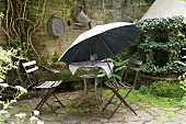 Alter Gartentisch mit Stühlen und Sonnenschirm auf Natursteinterrasse im Hinterhof