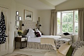 A spacious bedroom a high stack of light grey cushions on a double bed in front of a window