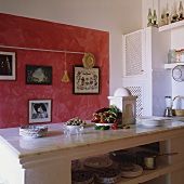 A Mediterranean kitchen - a marble surface on a white stone kitchen island in front of a sponged-painted red wall
