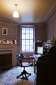 A study with wood panelled walls and an old wooden office chair in front of a Davenport