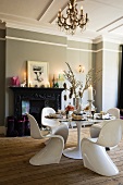 An elegant dining room with Bauhaus-style white plastic chairs and a table in front of a fireplace