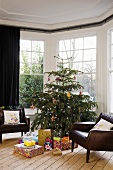 A leather armchair next to a decorated Christmas tree with presents in the bay window of a living room