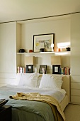 A white bedroom with a double bed in front of a self set into a wall niche