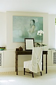 Bambustisch mit weißem Hussen Stuhl vor Wand mit Bild