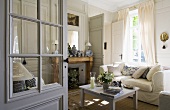 A view through an open door onto a comfortable white upholstered sofa with a county house-style coffee table