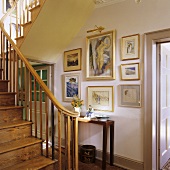 An old wooden staircase and a collection of pictures above a wall table in a stairwell in a country house