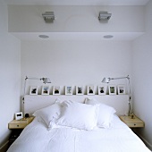 A bed with white bedclothes and a picture gallery in a wall niche and pivotable table lamps