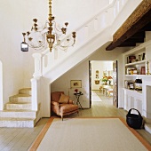 Offener Vorraum in Finca mit weißem Treppenaufgang und Barocksessel in der Treppennische mit Blick durch offene Tür
