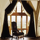 An antique armchair in front of a window with black curtains in the attic of a country house