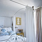 A bedroom in a country house with an antique metal bed and a canopy