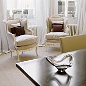Zwei hellgraue Sessel im Rokokostil vor Fenster mit luftigem bodenlangen Vorhang