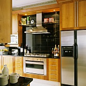 Wooden kitchen cupboards and a built-in cooker with an extractor fan against black wall tiles