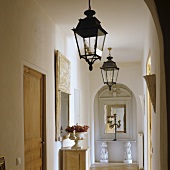 Foyer in a Provencal house with lanterns hanging from the ceiling and a view through rounded arches on an antique console table with a mirror
