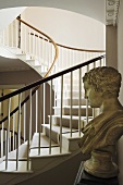 A bust and a curved stairway in the background