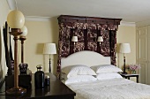 Englischer Schlafraum mit Tisch- und Wandlampen um das Doppelbett mit gemustertem Baldachin und weisser Bettwäsche
