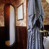 A bathroom with patterned wallpaper and a striped bathrobe hanging next to the open shower cubicle