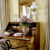Antique secretary with white kerosene lamp in front of a wall with yellow tones
