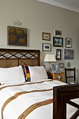 An antique wooden bed in front of a grey wall hung with a collection of pictures