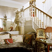 A grey velvet sofa and a bust in front of a wall mirror and a flight of white wooden stairs