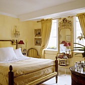 An elegant bedroom with an antique bed and a mirror with a gold frame on a yellow-painted wall