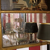 A table lamp with a black shade in front of an antique wall mirror
