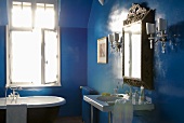 A blue bathroom - a designer washstand with an antique mirror and an old bathtub against a window
