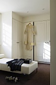 A built-in wardrobe in a dressing room with clothing on a white leather lounger