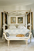 A white, antique painted four poster bed and a bench in a Mediterranean bedroom