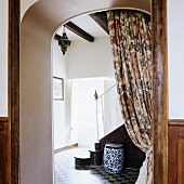 A view through an arched doorway with a floral-patterned curtain into an anteroom in a country house