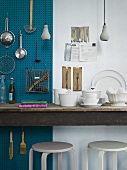 An arrangement of hanging kitchen utensils and white designer crockery on a wooden table