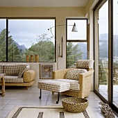 A wicker armchair with cushions and a footstool in the corner of a living room with a panoramic view