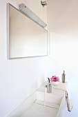 A corner of a bathroom - water running into white wash basin and a mirror with wall lighting