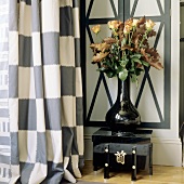 Roses in a black shiny vase on an Oriental box next to a checked curtain