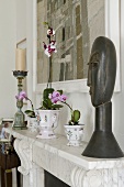 A carved wooden bust and orchids on a marble mantelpiece