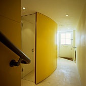 A curved cupboard with a yellow front and a mirrored door on the side in a hallway