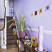A wall table at the foot of a flight of carpeted stairs in a lilac hallway