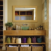 A light wood washstand built into a wall niche with baskets on the shelf below and a mirror above