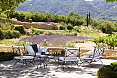 A terrace with metal chairs and cushions and a view of the Mediterranean landscape