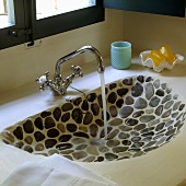 Water flowing from a vintage tap into a stone wash basin set with stones