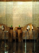 A mirrored hallway with a view of a wooden designer bar table and a bar stool against a natural stone wall