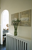 A vase of flowers on a concealed radiator and a arched doorway with a view into the bathroom