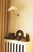 An arrangement of geometric wooden shaped on a covered radiator with a wall lamp above it