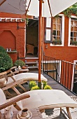 Loungers on a roof terrace with a view of a red facade and through an open door